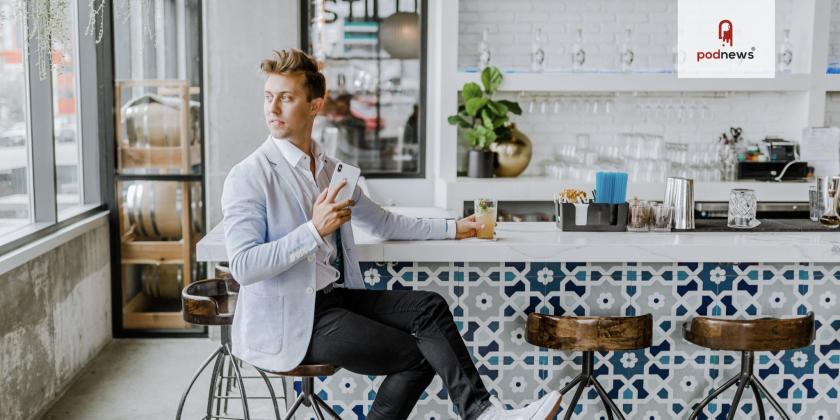 A bloke wearing a suit in a bar, holding a phone. We'd like to think he's listening to podcasts.