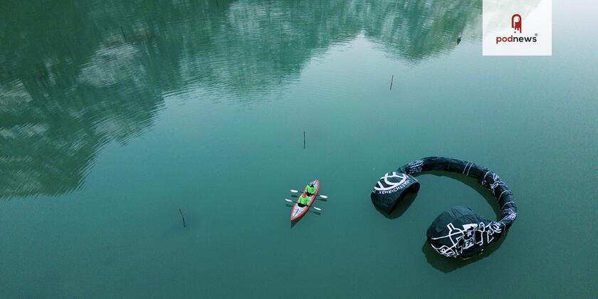 A canoe near an inflatable pair of headphones in a big green lake