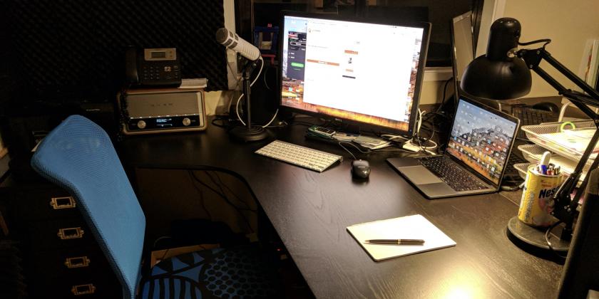 My office, with a MacBook and a monitor on the table, and a small microphone.